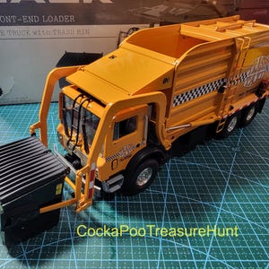May include: A detailed model of a yellow refuse truck with a black trash bin. The truck features a front-end loader design and the text "MR FRONT-END LOADER REFUSE TRUCK with TRASH BIN" is visible on the box. The truck has a checkerboard pattern.