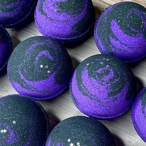 May include: Purple and black bath bombs with a galaxy swirl design. The bath bombs have a glittery finish.
