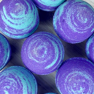 May include: A group of six bath bombs with a swirling blue and purple pattern. The bath bombs are round and have a textured surface.