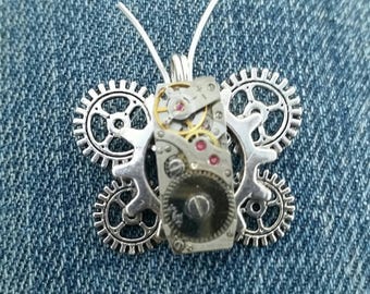 May include: Silver butterfly pendant with a clockwork design. The butterfly has two sets of gears on each side and a clock face in the center.