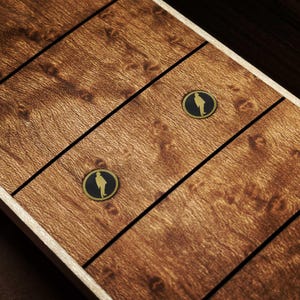 May include: A close-up shot of a wooden surface with a warm brown hue. The wood grain is visible, with dark lines dividing the panels. Two circular, gold-edged black emblems, each featuring a person's silhouette, are present.