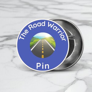 May include: A blue button with the text "The Road Warrior Pin" and a graphic of a road with a yellow line down the center.