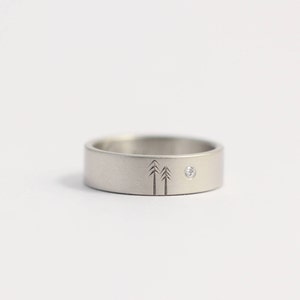 Peut inclure: Une bague en argent avec un petit diamant et un motif gravé de deux sapins.