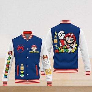 Op de afbeelding: Een blauw en wit Super Mario varsity jack. De jas heeft een rode kraag en manchetten met witte strepen. De voorkant heeft een groot "M" logo en een Mario afbeelding. De mouwen hebben "Super Mario" tekst en speliconen. De achterkant toont een grote Mario afbeelding.