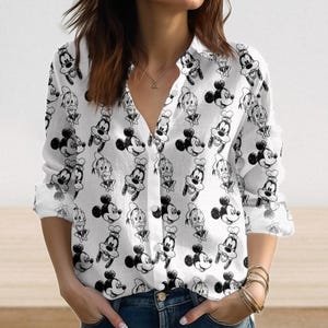 Może przedstawiać: Biała koszula zapinana na guziki z powtarzającym się czarno-białym wzorem Myszki Miki, Kaczora Donalda i Goofy'ego. Koszula z długim rękawem ma dekolt w serek i jest wykonana z lekkiego materiału.