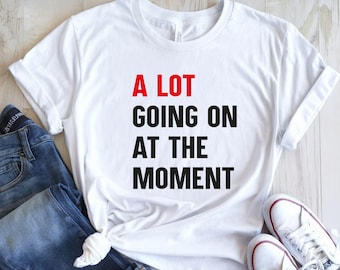 May include: White t-shirt with black text that reads "A LOT GOING ON AT THE MOMENT". The word "LOT" is in red.