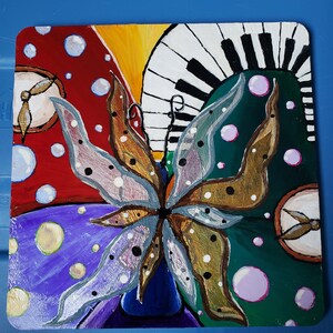 May include: A colorful abstract painting featuring a butterfly with gold and silver wings, surrounded by circles and a piano keyboard. The painting is done on a wooden panel.