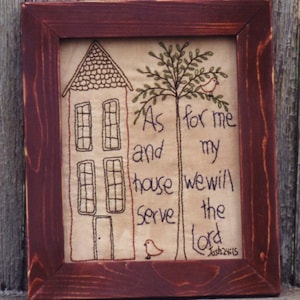 Op de afbeelding: Ingelijst kunstwerk met een bordeauxrode houten lijst. Het kunstwerk toont een gestikt ontwerp van een huis, een boom en vogels, met de tekst "As for me and my house we will serve the Lord Josh 24:15."