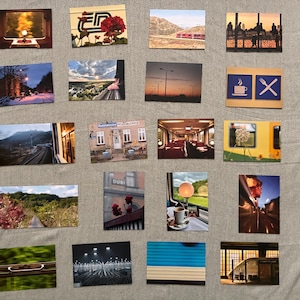 Könnte beinhalten: Eine Sammlung von neunzehn rechteckigen Postkarten mit verschiedenen fotografischen Motiven, darunter Zuginnenräume, Landschaften, Stadtansichten und Reisebilder, die in einem Rastermuster auf einem neutralfarbenen Stoff angeordnet sind.