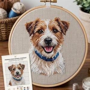 May include: A Jack Russell Terrier portrait cross-stitch pattern displayed in a wooden embroidery hoop. The dog has brown and white fur, a blue collar, and a happy expression. A smaller version of the pattern is shown on a card.