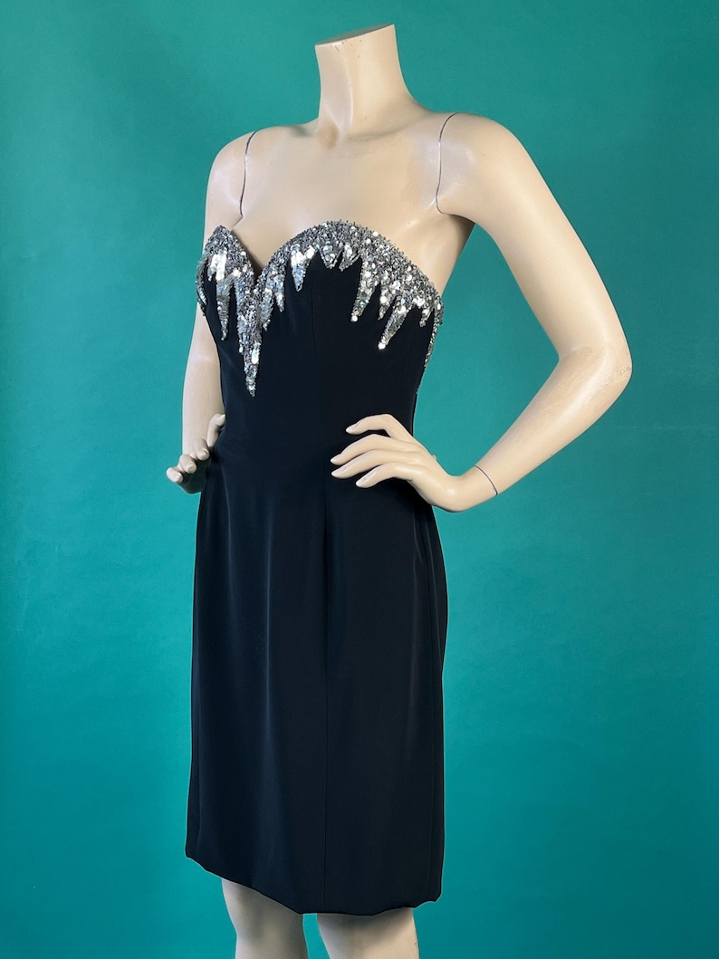 May include: A black strapless dress with a silver sequined bodice. The sequins are arranged in a cascading pattern.