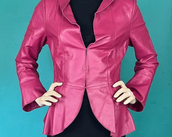May include: A magenta leather jacket with a flared peplum and a notched collar. The jacket has long sleeves and is displayed on a mannequin. The mannequin is wearing a black top and a black skirt. The background is a teal color.