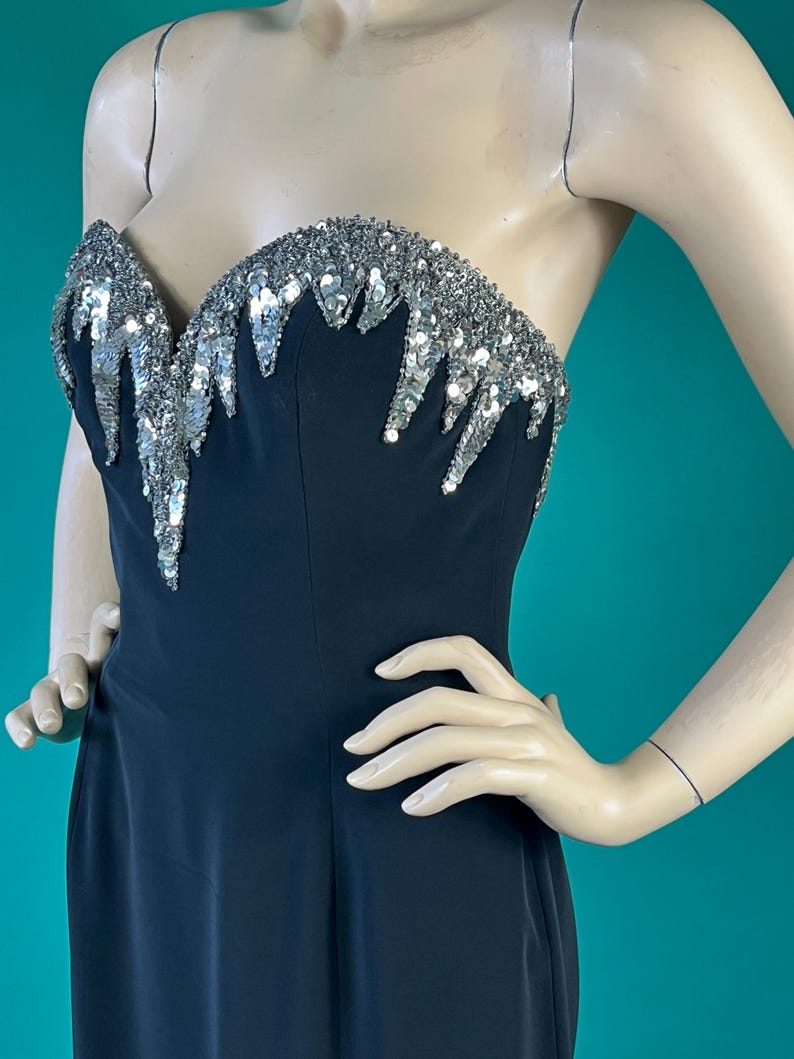 May include: A black strapless evening gown with a silver sequined bodice. The sequins are arranged in a cascading pattern.