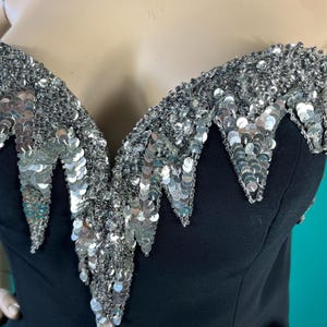 May include: A black strapless top with a silver sequined neckline. The sequins are arranged in a cascading pattern, creating a dramatic and eye-catching look.