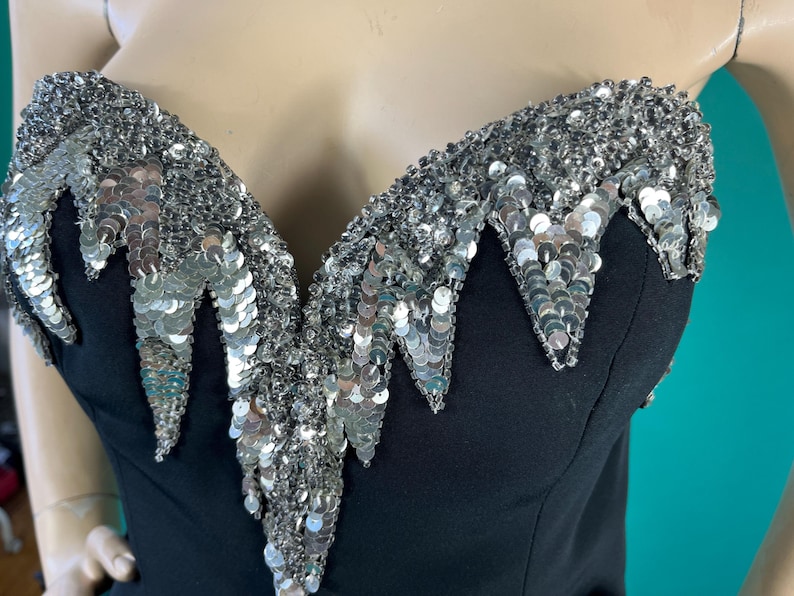 May include: A black strapless top with a silver sequined neckline. The sequins are arranged in a cascading pattern, creating a dramatic and eye-catching look.
