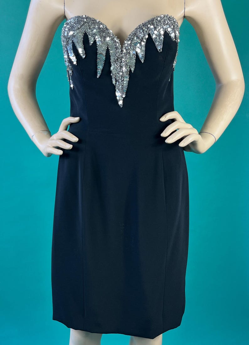 May include: A black strapless dress with a silver sequined bodice. The sequins are arranged in a cascading pattern.