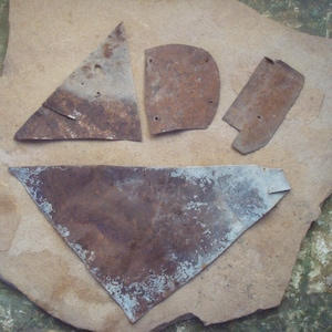 May include: A collection of irregularly shaped, rusty metal pieces. The pieces vary in size and shape, including a triangle, a half-circle, and a rectangle. The metal has a weathered appearance with areas of rust and discoloration, suggesting age and exposure to the elements.