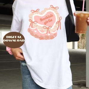 May include: White long-sleeve t-shirt with a pink heart-shaped graphic that says "Bookish girlie".