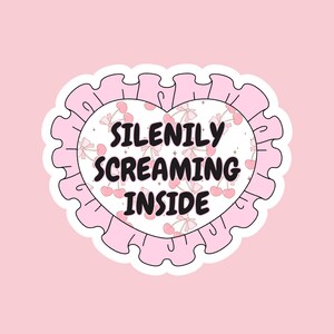 K&ouml;nnte beinhalten: Ein rosa herzf&ouml;rmiger Aufkleber mit wei&szlig;em Hintergrund und einem gekr&auml;uselten Rand. Der Aufkleber hat ein Kirschmuster und den Text "SILENILY SCREAMING INSIDE" in Schwarz.