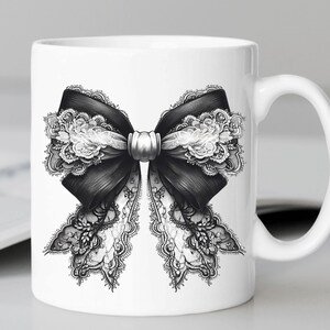 May include: White ceramic mug featuring a black and white lace bow design. The bow is tied with a silver ribbon.