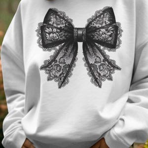 May include: White sweatshirt with a black lace bow design.
