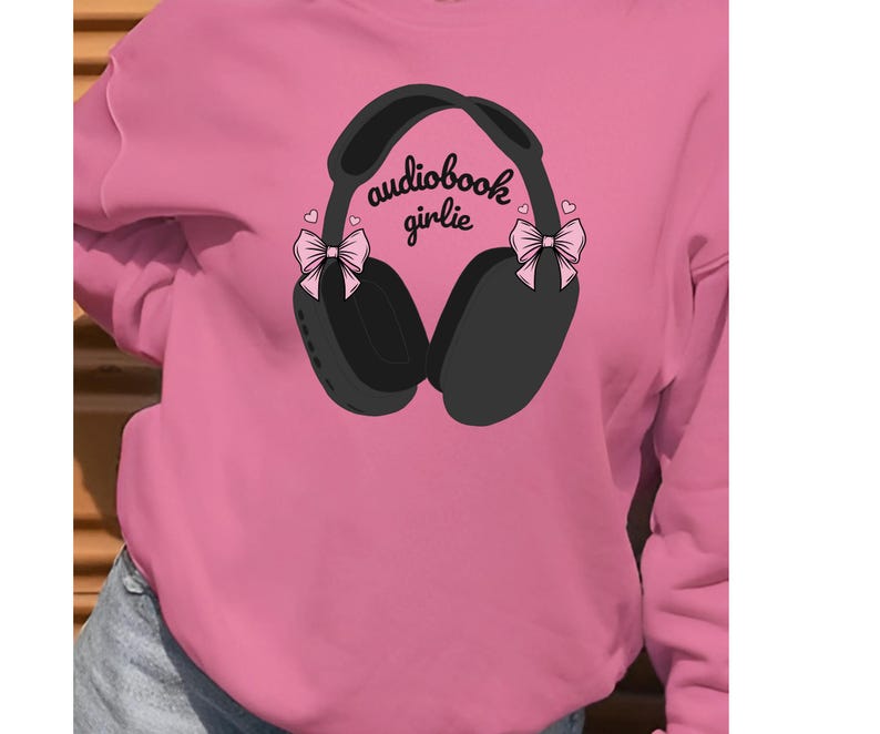 May include: Pink sweatshirt with a graphic of black headphones with pink bows on each side. The text "audiobook girlie" is printed on the headphones.