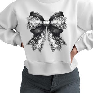 May include: A white cropped sweatshirt featuring a black and white lace bow design on the front.