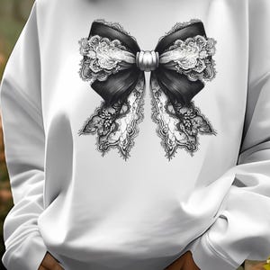 May include: White sweatshirt featuring a black and white lace bow design.