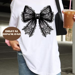 May include: A white t-shirt with a black lace bow design. The bow has a floral pattern and is centered on the shirt.