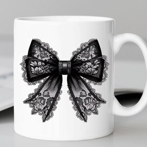 May include: White ceramic mug with a black lace bow design. The bow is detailed with intricate floral patterns.