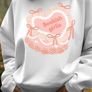 May include: White sweatshirt with a pink heart-shaped design and the text "Bookish girlie" in pink.