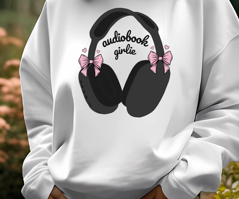 May include: White sweatshirt with a black and gray illustration of headphones with pink bows and the text "audiobook girlie".