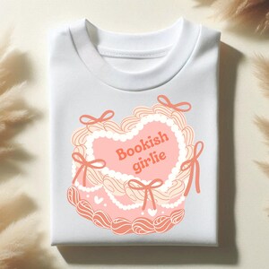 May include: White t-shirt with a pink and white heart-shaped design and the text "Bookish girlie" in orange.
