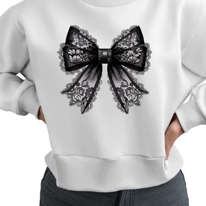 May include: White sweatshirt with a black lace bow design on the front.