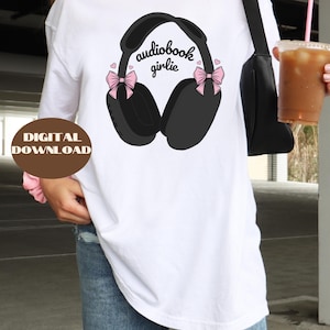 May include: White t-shirt with a black and white illustration of headphones with pink bows and the text "audiobook girlie".