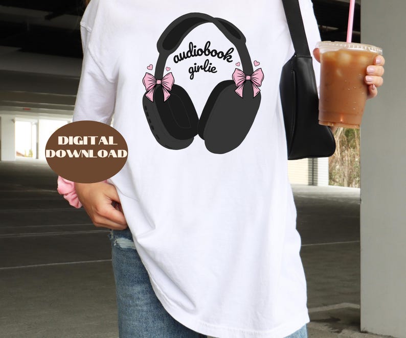 May include: White t-shirt with a black and white illustration of headphones with pink bows and the text "audiobook girlie".