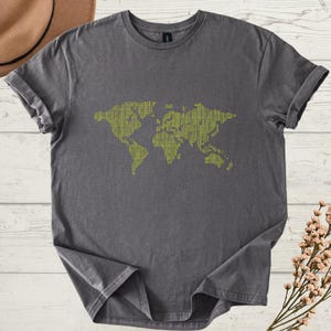 K&ouml;nnte beinhalten: Ein anthrazitfarbenes T-Shirt mit einem gr&uuml;nen Weltkarten-Design. Die Karte besteht aus einem sich wiederholenden Muster, das ein strukturiertes Aussehen erzeugt. Das T-Shirt hat kurze &Auml;rmel und einen Rundhalsausschnitt.