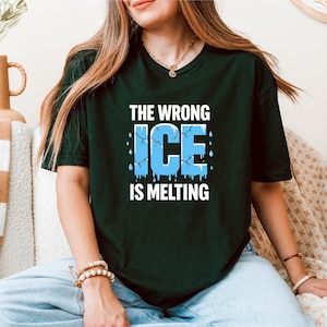 Puede incluir: Camiseta verde oscuro con el texto "THE WRONG ICE IS MELTING" en blanco y azul claro. La palabra "ICE" está diseñada para parecer hielo derritiéndose. La camiseta es de manga corta y cuello redondo.