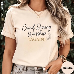 Puede incluir: Camiseta beige con el texto "Cried During Worship (AGAIN)" en escritura gris oscuro. La camiseta presenta un pequeño diseño de hojas y está hecha de un material suave. La camiseta es de color neutro.