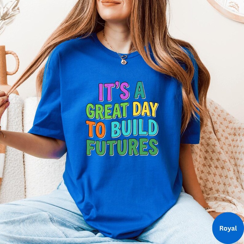 May include: Royal blue t-shirt with the text "IT'S A GREAT DAY TO BUILD FUTURES" in colorful block letters. The shirt is a short-sleeved crew neck style. The text is in pink, yellow, orange, and green.