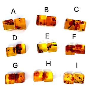 Könnte beinhalten: Neun Paar quadratische Bernsteinohrringe mit Einschlüssen aus rotem und braunem organischem Material. Jedes Paar ist mit einem Buchstaben von A bis I gekennzeichnet. Die Ohrringe haben einen warmen, goldenen Farbton und werden vor weißem Hintergrund präsentiert.