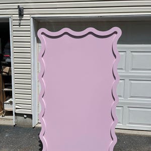 May include: A large, pink, wavy-edged backdrop for photography or events. The backdrop is made of a smooth, flat material and has a slightly textured surface.