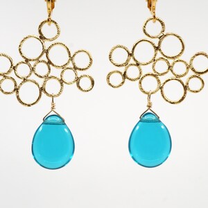 May include: Gold earrings with a cluster of interconnected circles and a dangling turquoise teardrop-shaped bead.