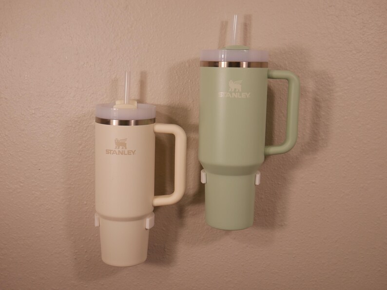 May include: Two stainless steel travel mugs with lids and straws. The mugs are green and beige and have the Stanley logo on them.