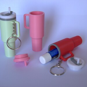 May include: Three keychain containers, one green, one pink, and one red, with a lip balm inside the red container. Each container has a small handle and a key ring.
