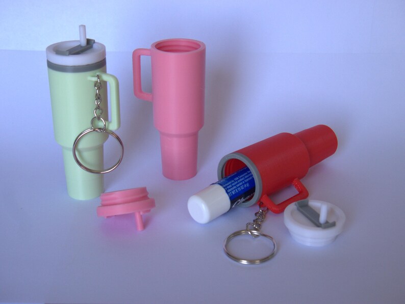 May include: Three keychain containers, one green, one pink, and one red, with a lip balm inside the red container. Each container has a small handle and a key ring.