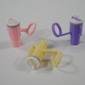 May include: Three colorful plastic sippy cup lids in pink, yellow, and purple. Each lid has a handle and a white and gray top with a small opening. The cups are designed for easy drinking and spill prevention.