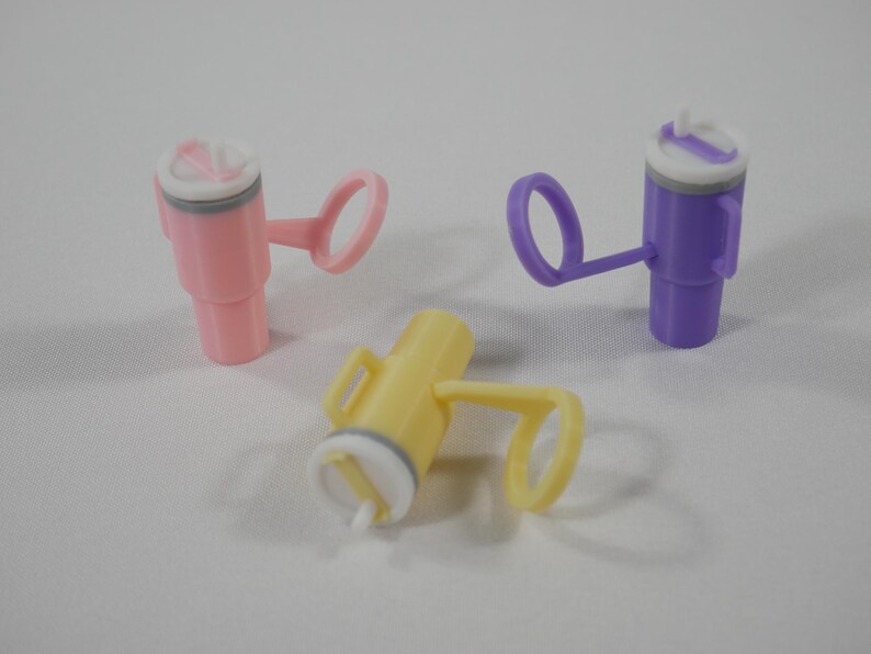 May include: Three colorful plastic sippy cup lids in pink, yellow, and purple. Each lid has a handle and a white and gray top with a small opening. The cups are designed for easy drinking and spill prevention.