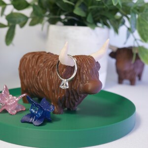 May include: A brown Highland cow figurine with white horns and a ring on its nose, sitting on a green circular tray with two blue butterfly hair clips and a pink butterfly hair clip.