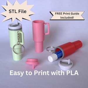 Op de afbeelding: Drie 3D-geprinte sleutelhanger-containers, een groen, een roze en een rood. De rode container is open en toont een lippenbalsem erin. De containers zijn gelabeld met "STL File" en "FREE Print Guide Included!" en "Easy to Print with PLA".